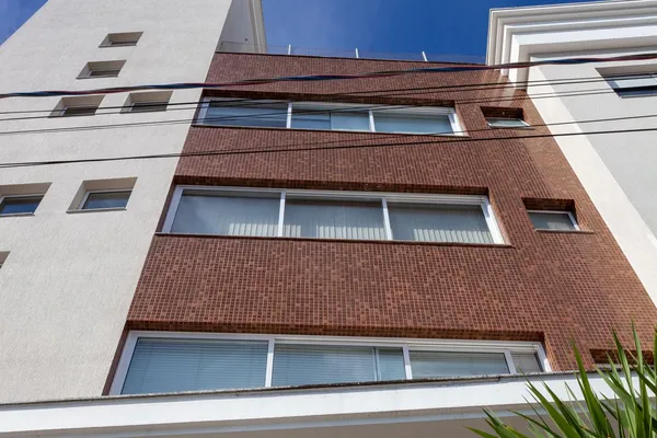 Fachada residencial moderna com esquadrias de alumínio pretas, amplas lâminas de vidro de segurança e vedação reforçada.